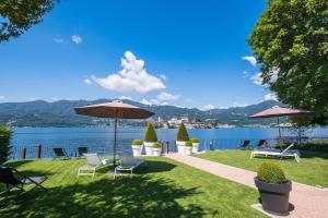 a lawn with chairs and umbrellas next to a lake at Bifora65 flats and garden - Lakeview in Orta San Giulio