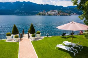 a lawn with an umbrella and chairs and a lake at Bifora65 flats and garden - Lakeview in Orta San Giulio
