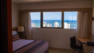 a bedroom with a window with a view of the ocean at Beach Class Convention By Hôm - Antigo Bristol Recife in Recife