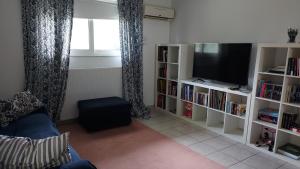 uma sala de estar com televisão e estantes de livros em Joan's airport apartment em Artemida