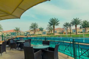 eine Terrasse mit Tischen und Stühlen neben einem Pool in der Unterkunft Swiss International Resort Unaizah Al Qassim in Unaizah
