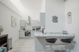 a white kitchen with two bar stools at a counter at Hullidays-Theatre Hideout Apartment in Hull