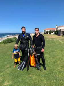 three men in wetsuits standing on the beach with a child at Whales & Waves in Hermanus