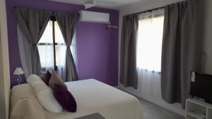 a bedroom with a white bed with purple walls and windows at Casas del Champaquí in San Javier