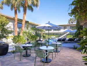 eine Terrasse mit Tischen, Stühlen und einem Sonnenschirm in der Unterkunft Descanso Resort, A Men's Resort in Palm Springs