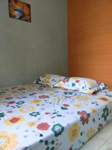 a bed with a floral comforter and pillows on it at Mandeh Guesthouse Padang in Padang