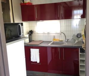 cocina con armarios rojos, fregadero y microondas en Chalet à deux pas de la plage, en Martigues