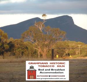 a sign in front of a tree with mountains in the background at Grampians Historic Tobacco Kiln in Moutajup