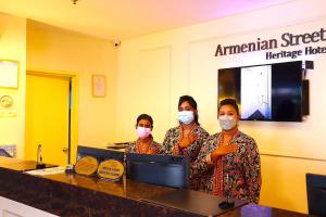 ジョージタウンにあるアルメニアン ストリート ヘリテージ ホテルのカウンターに立つ顔面を着た三人