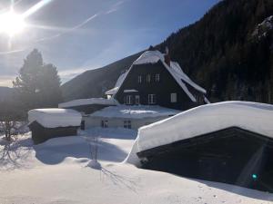 a house covered in snow with the sun behind it at Ankogel Lofts Mallnitz in Mallnitz