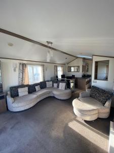uma sala de estar com um grande sofá e cadeiras em E3 is a 2 Bedroom 6 berth Lodge on Whitehouse Leisure Park in Towyn near Rhyl close to beach with decking and private parking space This is a pet free caravan em Rhyl