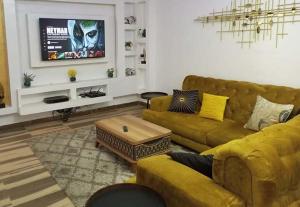 ein Wohnzimmer mit einem gelben Sofa und einem TV in der Unterkunft Westpark Luxury Apartments in Ikeja