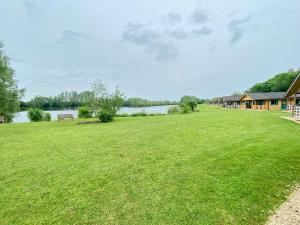 a large grassy yard with a house and a lake at Reeds Lodge, Lake Pochard in South Cerney