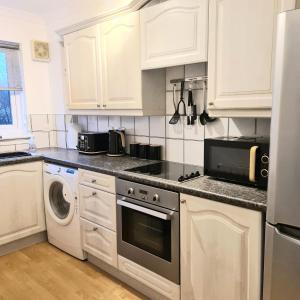 cocina con armarios blancos, lavadora y secadora en Levenside Holiday Apartment, Balloch, Loch Lomond, en Balloch