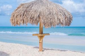 a straw umbrella on a beach with the ocean at Yoyita Suites Aruba Villa in Palm-Eagle Beach