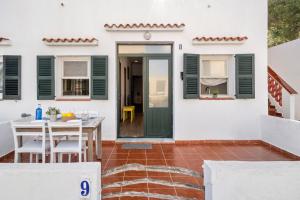 a white house with green doors and a table and chairs at Apartamento Sa Mesquida 9 in Cala Llonga
