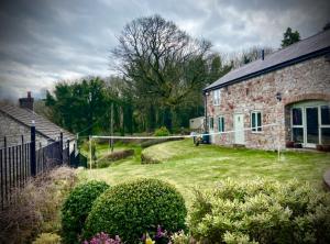 a stone house with a yard of grass and bushes at Parc Farm Cottage, Flintshire, North Wales in Rhydymwyn