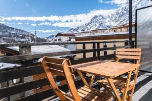 a wooden table and chairs on a balcony with snow covered mountains at Stay in Cervinia Deluxe Apartment in Breuil-Cervinia