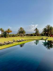 una piscina de agua con tumbonas y palmeras en DAR NOUJOUM en Marrakech