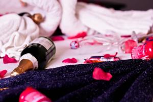 Una botella de vino sentada en una cama con rosas rojas en Hotel Al-Khalil Matola en Matola