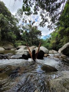 Une femme debout dans une rivière avec ses bras dans l'air dans l'établissement Pousada Camping dos Ypês, à Guapimirim