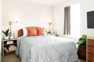 InTown Suites Extended Stay Clearwater FL في كليرووتر: غرفة نوم بيضاء مع سرير مع وسائد برتقالية