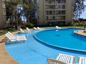 een zwembad met witte stoelen en een gebouw bij Depto en Costa Algarrobo Norte con wifi in Algarrobo
