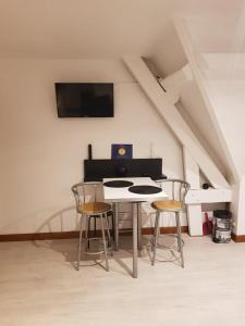 een tafel met twee stoelen en een tv aan de muur bij Hibiscus 1er étage in Honfleur