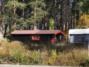 una piccola baita di tronchi con tetto rosso accanto a una foresta di Båtstø Camping a Elga