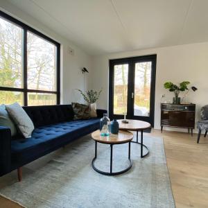 een woonkamer met een blauwe bank en 2 tafels bij Huisje Hygge - luxe bungalow met grote tuin in Ewijk