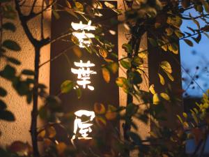 a building with a lit up sign behind a tree at Guest House Wakabaya in Takamatsu