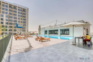 una piscina con bancos, una sombrilla y un parque infantil en Urban Studio at UNA Town Square Dubailand By Deluxe Holiday Homes en Dubái