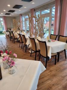 une salle à manger avec des tables blanches, des chaises et des fleurs dans l'établissement Land-gut-Hotel Waldesruh, à Altenmedingen