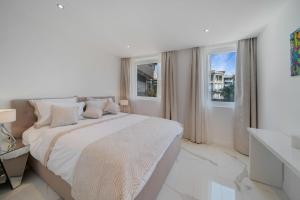 a white bedroom with a large bed and two windows at Appartements Croisette Grand Hôtel in Cannes