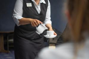 una mujer sosteniendo una taza de café en un plato en City Club Hotel, en Oldenburg