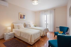 a white bedroom with two beds and a blue chair at Exclusive Center Apartments in Zadar