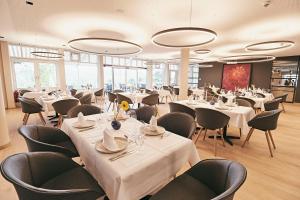 ein Restaurant mit weißen Tischen und Stühlen und Fenstern in der Unterkunft Seehotel Maria Laach in Maria Laach