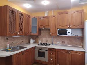 cocina con armarios de madera, fregadero y microondas en Уютная однокомнатная квартира в г. Бровары, en Brovary