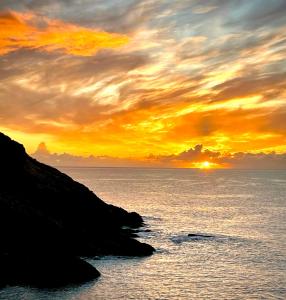a sunset over the ocean with a rocky shoreline at Unique Retreat - 2 bedroom cliff top cottage with large terrace in Portloe
