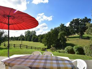 una mesa y sillas con una sombrilla roja y un campo en Cosy chalet with private garden in Normandy, en Isigny-le-Buat