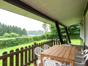 une terrasse couverte avec une table en bois et des chaises blanches dans l'établissement Detached chalet with views of the lake of Butgenbach in the middle of nature, à Butgenbach