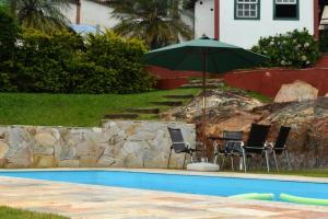 una mesa con sillas y una sombrilla junto a la piscina en Pousada Villa Verde, en Lavras Novas