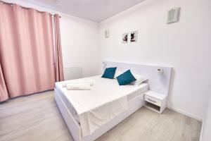 a white bedroom with a white bed with blue pillows at Ana Apartament in Năvodari