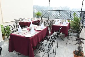 un groupe de tables avec des nappes rouges sur un balcon dans l'établissement Auckland Hotel and Restaurant Near Mall Road, à Shimla