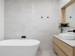 a white bathroom with a tub and a sink at Ocean Scene in Fingal Bay