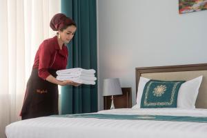 a woman holding a pile of towels next to a bed at Hotel Shumon in Dushanbe