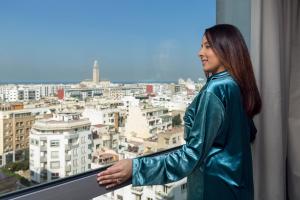 Una donna con una giacca di pelle verde che guarda fuori da una finestra di Idou Anfa Hôtel & Spa a Casablanca