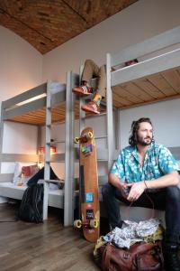 Ein Mann, der auf einem Etagenbett mit einem Skateboard sitzt. in der Unterkunft Pfefferbett Hostel in Berlin