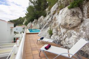 balcón con sillas blancas y pared de roca en Cala Galdana Apartamentos El Rio 1 habitación, en Cala Galdana