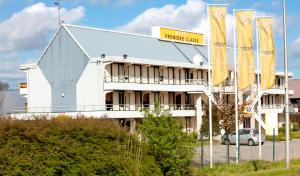 un bâtiment avec des drapeaux jaunes devant lui dans l'établissement Premiere Classe Dunkerque Est Armbouts Cappel, à Armbouts-Cappel